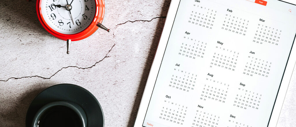a tablet with an open calendar for 2021 year, a cup of coffee, and a red alarm clock on a gray concrete background. banner